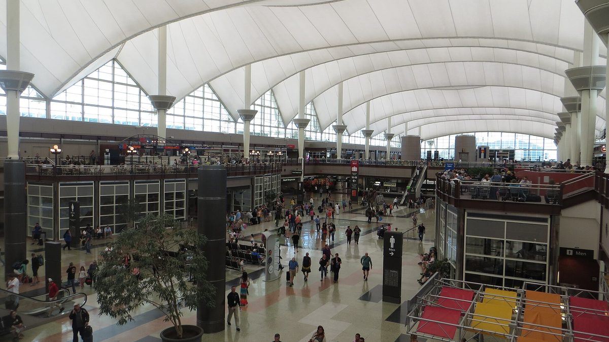 The Jeppesen Terminal at Denver International Airport, with travelers walking through the main concourse under its tented roof