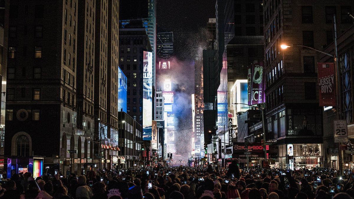 Crowds filling the streets around Times Square in New York City on New Year's Eve, with confetti falling under bright billboards