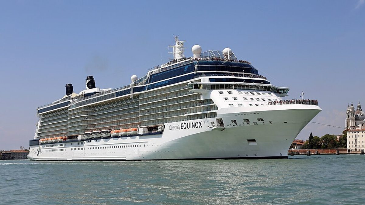 Celebrity Equinox at sea with passengers lining the top decks, sailing past a historic waterfront