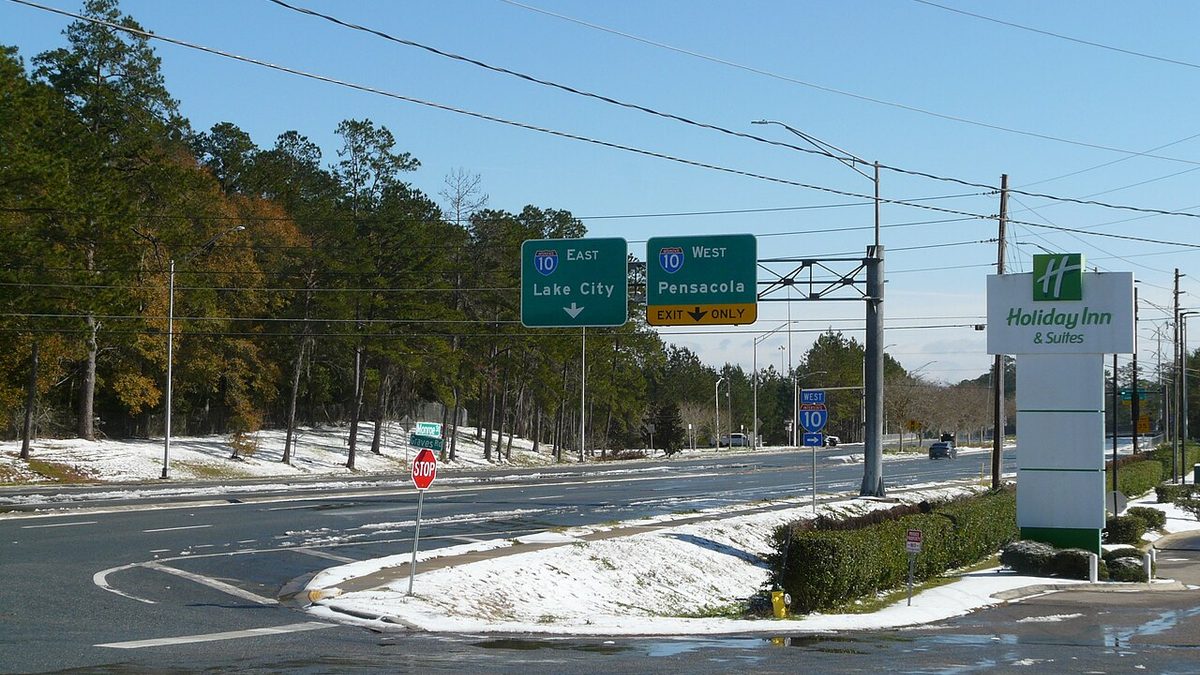 A snow-covered roadside on US 27 near Interstate 10 in Tallahassee, Florida, on 22 January 2025, with a highway sign pointing toward Pensacola
