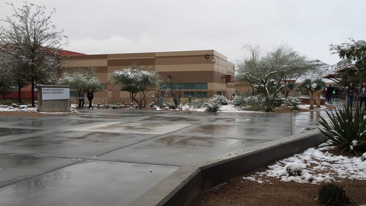 Snow covering trees, desert plants and sidewalks at a Las Vegas school campus, with students walking past in light jackets