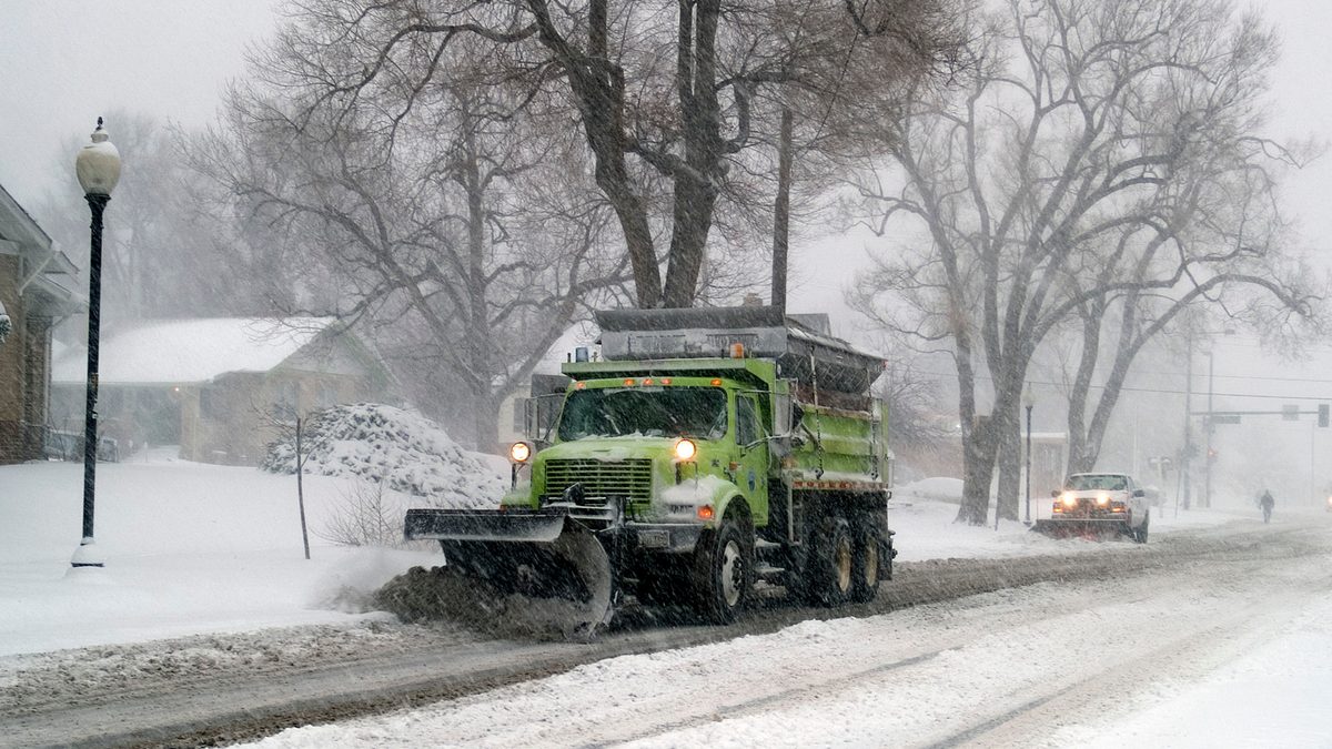 A snowplough clearing a Colorado street past a tavern during heavy falling snow