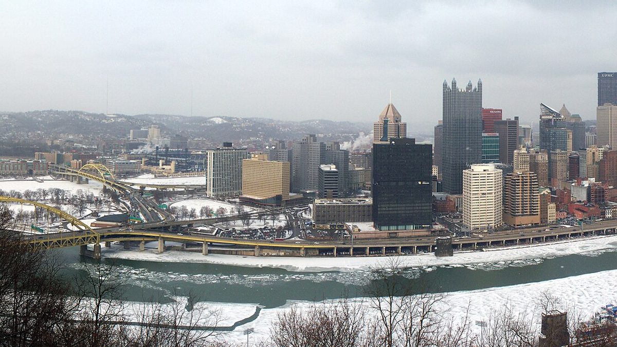 Downtown Pittsburgh under snow, with ice on the Monongahela River and the yellow Fort Pitt Bridge in the foreground
