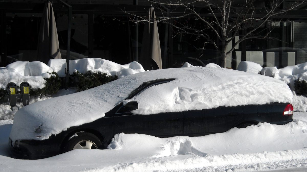A car parked on a residential street buried under a fresh layer of snow