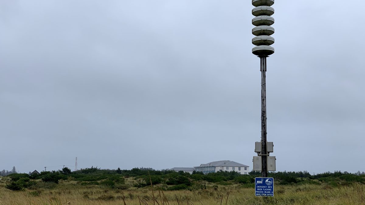 A NOAA tsunami warning siren on the Washington coast, with a sign reading proceed inland and away from water