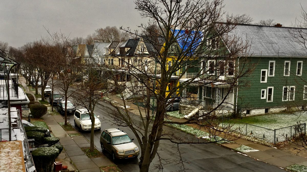 A light dusting of early-season snow on a residential Buffalo, New York street, with bare trees and parked cars